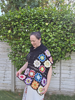 Black lace rectangular shawl with bright floral granny square border at short ends worn wrapped over shoulder