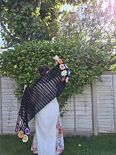 Black lace rectangular shawl with bright floral granny square border at short ends held diagonally behind wearer