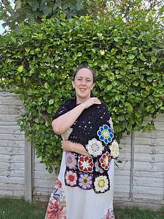 Black lace rectangular shawl with bright floral granny square border at short ends worn wrapped over shoulder