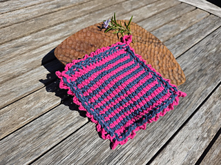 Pink and navy crocheted cloth with a purple rosemary flower and leaves on a sunlit wooden table