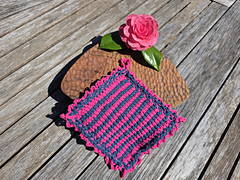 Pink and navy crocheted cloth with a pink camellia flower and leaves on a sunlit wooden table