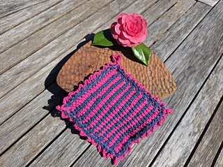 Pink and navy crocheted cloth with a pink camellia flower and leaves on a sunlit wooden table