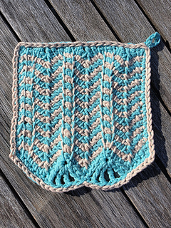 Turquoise and beige striped chevron stitch crocheted cloth on a wooden table in sunny outdoor setting
