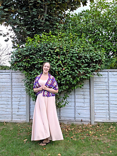 crochet lace shawl with colourful butterfly design  in blues purples, pinks and green on a woman in a leafy garden (front)