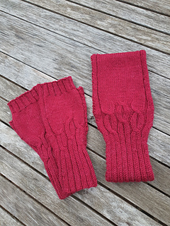 Deep red cable knitted headband and matching pair of fingerless gloves (not included in Headband pattern) lying on a weathered grey wooden slatted table.