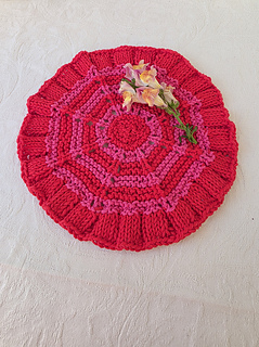 Red knitted circular washcloth with pink stripes with flowers on a white textured cloth.