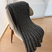 The Cloud Blanket — charcoal wool, draped over a woven chair.