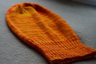 View of a semi-solid orange knit Sockhead hat lying flat.