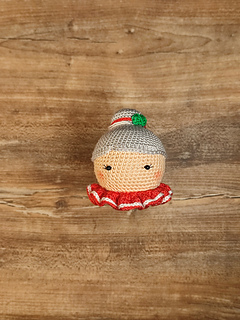 Crochet Mrs. Claus doll wearing a red collar with white details and gray hair in a bun. Put on the table.