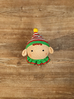 Handmade crochet Christmas elf with pointed hat, striped outfit, and playful expression. Put on the table.