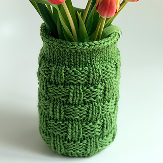 Green knitted mason jar cozy with tulips on a white background.