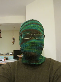 Person wearing a green Sockhead hat pulled down completely over face with glasses worn overtop.