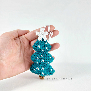 A hand-crocheted Christmas tree with imitation snow and a 'snowflake' on top, held in a hand, showing its size, made from a step-by-step pattern.