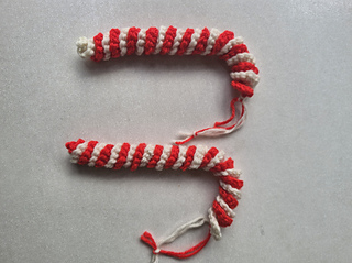 Long crocheted red and white striped candy cane ornament lying on a light surface