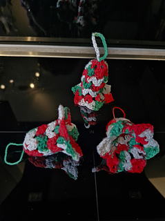 Crocheted red, green and white Christmas bell ornaments on a dark reflective surface