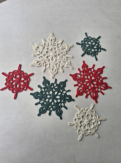 Set of crocheted snowflake ornaments in cream, dark green and red on a light surface