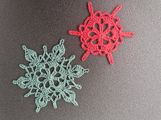 Two crocheted snowflake ornaments in coral red and mint green on a dark surface